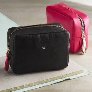 May include: Two leather cosmetic bags, one black with gold initials "CW" and one hot pink. Both bags have gold zips and tassels.