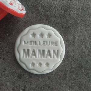 Puede incluir: Sello para galletas blanco con el texto "MEILLEURE MAMAN" rodeado de cinco estrellas.