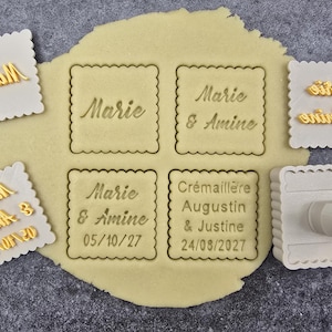 Puede incluir: Un conjunto de sellos para galletas e impresiones en masa. Los sellos blancos, con bordes festoneados, presentan nombres y fechas. La masa tiene impresiones de los nombres "Marie" y "Amine".