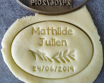 May include: A brown plastic cookie cutter with the text "Mathilde Julien 24/06/2019" and a branch design. The cookie cutter is used to create a cookie with the same design.