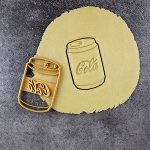 Puede incluir: Dos cortadores de galletas con forma de lata de refresco. Los cortadores de galletas est&aacute;n hechos de metal y tienen un acabado plateado. Los cortadores de galletas est&aacute;n sobre una superficie marr&oacute;n claro.