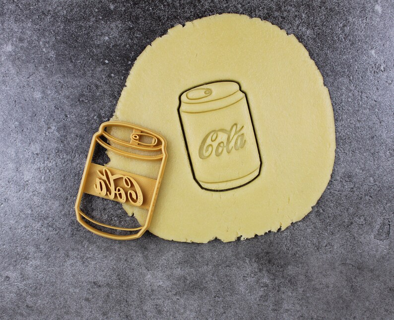 Puede incluir: Dos cortadores de galletas con forma de lata de refresco. Los cortadores de galletas est&aacute;n hechos de metal y tienen un acabado plateado. Los cortadores de galletas est&aacute;n sobre una superficie marr&oacute;n claro.