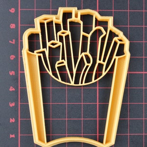 Puede incluir: Un cortador de galletas de pl&aacute;stico amarillo con forma de un contenedor de patatas fritas. El cortador est&aacute; dise&ntilde;ado para cortar una forma de un contenedor de patatas fritas.