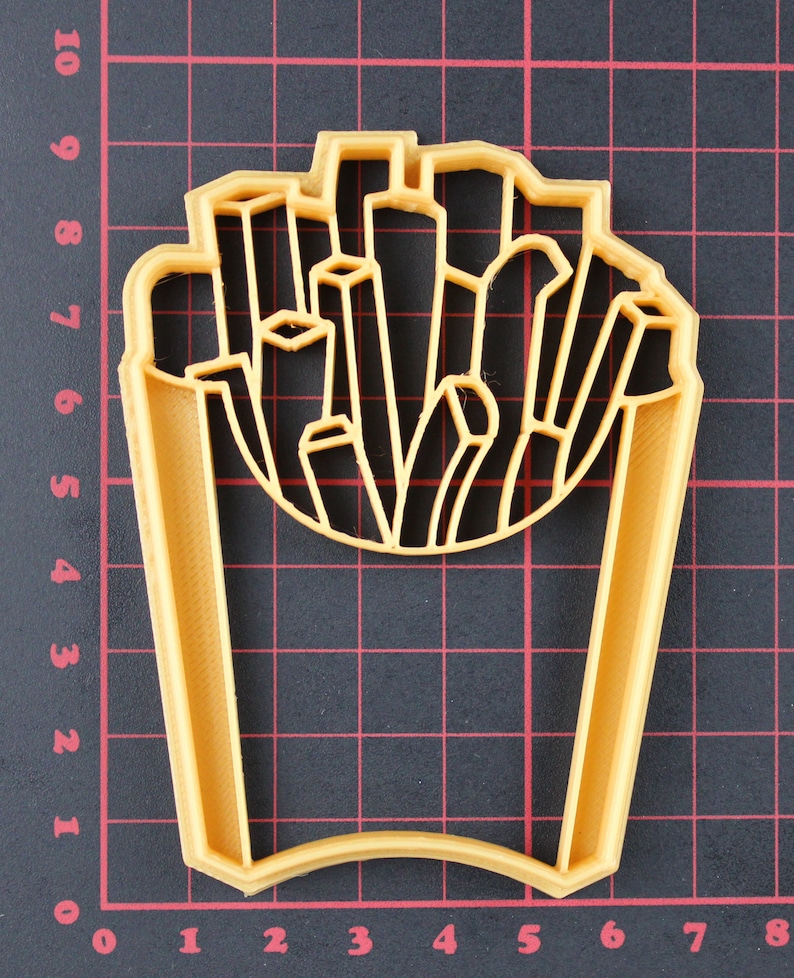 Puede incluir: Un cortador de galletas de pl&aacute;stico amarillo con forma de un contenedor de patatas fritas. El cortador est&aacute; dise&ntilde;ado para cortar una forma de un contenedor de patatas fritas.