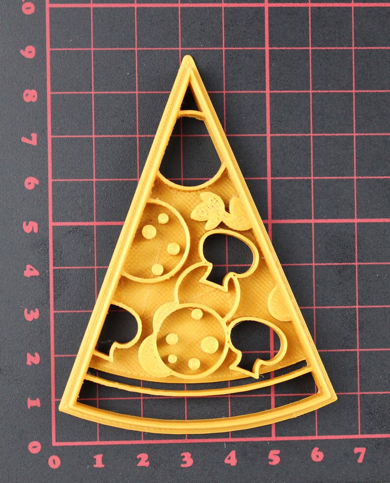 Puede incluir: Un cortador de galletas de pl&aacute;stico amarillo en forma de rebanada de pizza con un dise&ntilde;o detallado de pepperoni, champi&ntilde;ones y queso.