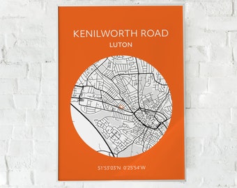 May include: An orange framed print with a map of Kenilworth Road, Luton. The map is in a white circle, with black lines representing streets and buildings. The text "KENILWORTH ROAD LUTON" is at the top, and coordinates are at the bottom.
