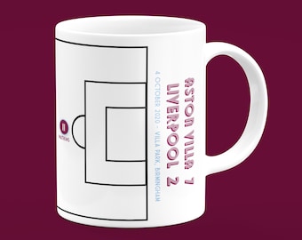 May include: White ceramic mug with a black and white football field graphic. The text "Aston Villa 7 Liverpool 2" is printed on the side of the mug in pink with a shadow effect. The date "4 October 2020 - Villa Park, Birmingham" is printed in blue below the score.