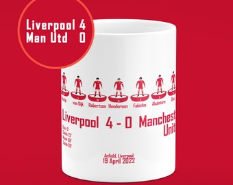 May include: White ceramic mug with a red and white illustration of a soccer team lineup. The text "Liverpool 4 - 0 Manchester United" is printed on the mug. The date "19 April 2022" is also printed on the mug.