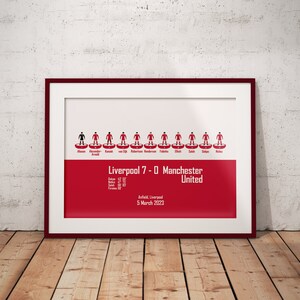 May include: A framed print of a football match lineup, showing the Liverpool team that won 7-0 against Manchester United on March 5, 2023 at Anfield. The print features a red background with the team's lineup in a classic football formation.