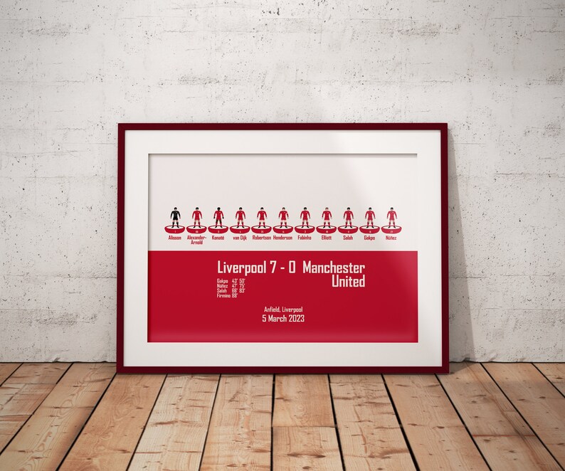 May include: A framed print of a football match lineup, showing the Liverpool team that won 7-0 against Manchester United on March 5, 2023 at Anfield. The print features a red background with the team's lineup in a classic football formation.