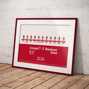 May include: A red and white framed print of a football match lineup. The print shows the Liverpool team lineup for their 7-0 victory over Manchester United on March 5, 2023. The players are represented by red and white stick figures.
