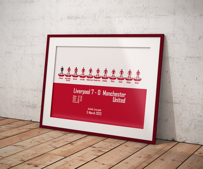 May include: A red and white framed print of a football match lineup. The print shows the Liverpool team lineup for their 7-0 victory over Manchester United on March 5, 2023. The players are represented by red and white stick figures.