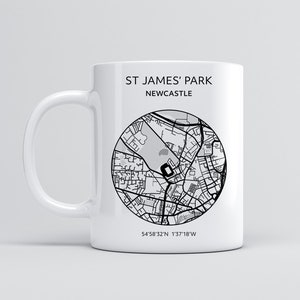 Pu&ograve; includere: Una tazza in ceramica bianca con una mappa in bianco e nero di St. James' Park, Newcastle, Inghilterra. La tazza ha il testo "St. James' Park Newcastle" e le coordinate "54&deg;58'32"N 1&deg;37'18"W" stampate su di essa.