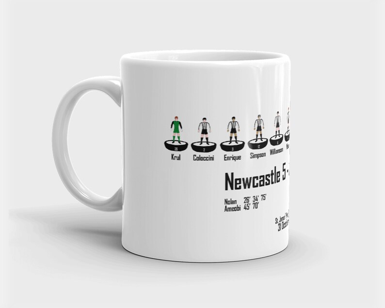 K&ouml;nnte beinhalten: Eine wei&szlig;e Keramiktasse mit einer Schwarzwei&szlig;illustration einer Fu&szlig;ballmannschaft. Die Tasse zeigt die Namen Krul, Coloccini, Enrique, Simpson und Williamson. Der Text "Newcastle 5" ist unter der Aufstellung gedruckt. Der Text "Nolan 26&deg; 34' 75" und "Ameobi 45 70" ist unter dem Teamnamen gedruckt.