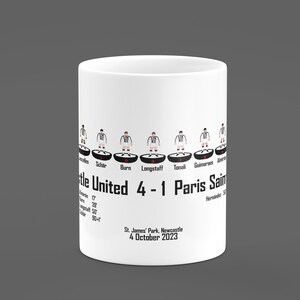May include: White ceramic mug with a black and white illustration of a soccer lineup. The text "Newcastle United 4-1 Paris Saint" is printed on the mug. The date "4 October 2023" and the location "St. James' Park, Newcastle" are also printed on the mug.