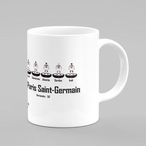 May include: White ceramic mug with a black and white illustration of a soccer team lineup. The team name "Paris Saint-Germain" is printed below the lineup. The players are wearing black and white uniforms.