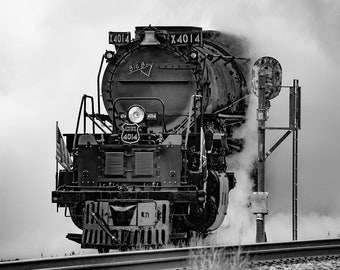 May include: A black and white photo of a large steam locomotive, known as "Big Boy", with the number "4014" on the front. The locomotive is emitting a large plume of steam, and the photo is taken from a low angle, looking up at the locomotive.