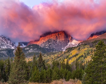 May include: A mountain peak with a pink and orange cloud cover, a stream flows through a forest with fall foliage.