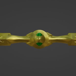 May include: A gold-colored metal decorative piece with a green gemstone in the center. The piece has a symmetrical design with two pointed ends.