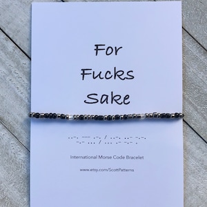 May include: A white card with black text that reads "For Fucks Sake" and a black and silver beaded bracelet with the phrase in Morse code below. The text "International Morse Code Bracelet" and a website address are printed below the Morse code.