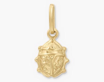 Könnte beinhalten: Ein goldener Anhänger in Form eines Marienkäfers mit polierter Metalloberfläche, geprägten kreisförmigen Details auf den Flügeln und einem glatten, abgerundeten Kopfbereich. Der Anhänger besitzt oben einen kleinen, vertikalen Ring.