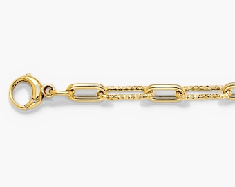 May include: A gold chain bracelet featuring elongated oval links with a polished finish alternating with textured, diamond-cut links. The bracelet includes a secure lobster claw clasp at one end, showcasing a bright, reflective metallic yellow tone.