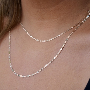 A model elegantly wears the 14K solid gold Valentino chain necklace, showcasing its refined, lightweight design. The 2mm and 3mm chains drape gracefully around the neck, highlighting their polished gold shine. Perfect for everyday wear or special occasions, these Italian-made chains exude timeless sophistication and versatility.
