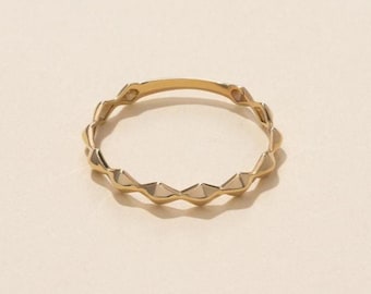 May include: A thin gold ring featuring a continuous series of small, raised, diamond-shaped geometric facets along the entire outer circumference of the band, creating a textured, repeating pattern with a polished metallic finish.