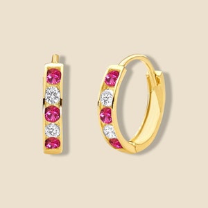 May include: Gold hoop earrings with a row of pink and white gemstones.