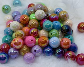 May include: A collection of iridescent round beads in various colors, including pink, blue, green, and purple. Each bead has a hole for stringing and a glossy finish. The beads are scattered on a white, fluffy surface.
