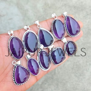 May include: A collection of amethyst pendants in various shapes, including oval, teardrop, and square. Each pendant features a polished, deep purple gemstone set in a silver-toned metal frame. The pendants are displayed on a hand.