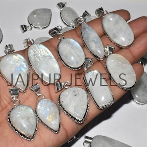 May include: A collection of 12 silver pendants with moonstone gemstones. The pendants are various shapes and sizes, including teardrop, oval, and rectangular. The moonstone gemstones are white with iridescent flashes of color.