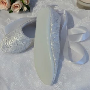 May include: A pair of white satin bridal shoes with a floral pattern and white satin ribbon ties.