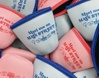 Könnte beinhalten: Eine Sammlung von isolierten Getränke-Hüllen in Rosa- und Hellblautönen. Jede Hülle trägt den Text "Meet me on MAIN STREET" mit Illustrationen. Die Hüllen haben kontrastierende blaue und rosa Verzierungen.