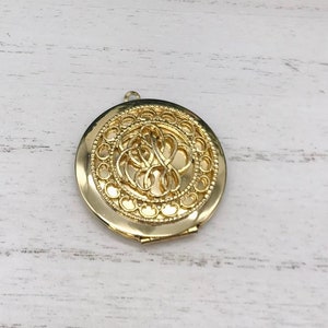 May include: A gold locket with a filigree design. The locket is closed and has a small loop at the top for attaching a chain.