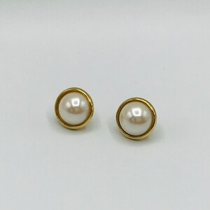 May include: A pair of gold-toned stud earrings with a white pearl center.