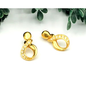 May include: Gold tone earrings with a twisted design and clear rhinestones.