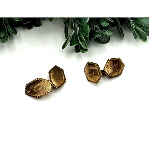 May include: Two pairs of vintage gold-toned cufflinks with a geometric design. The cufflinks have an octagonal shape with etched details. The background is white with green foliage at the top, creating a classic and elegant aesthetic.