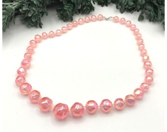May include: A pink iridescent beaded necklace with a silver clasp. The beads are faceted and have a slightly irregular shape.