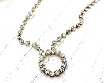 May include: A silver necklace with a circle pendant made of clear rhinestones.