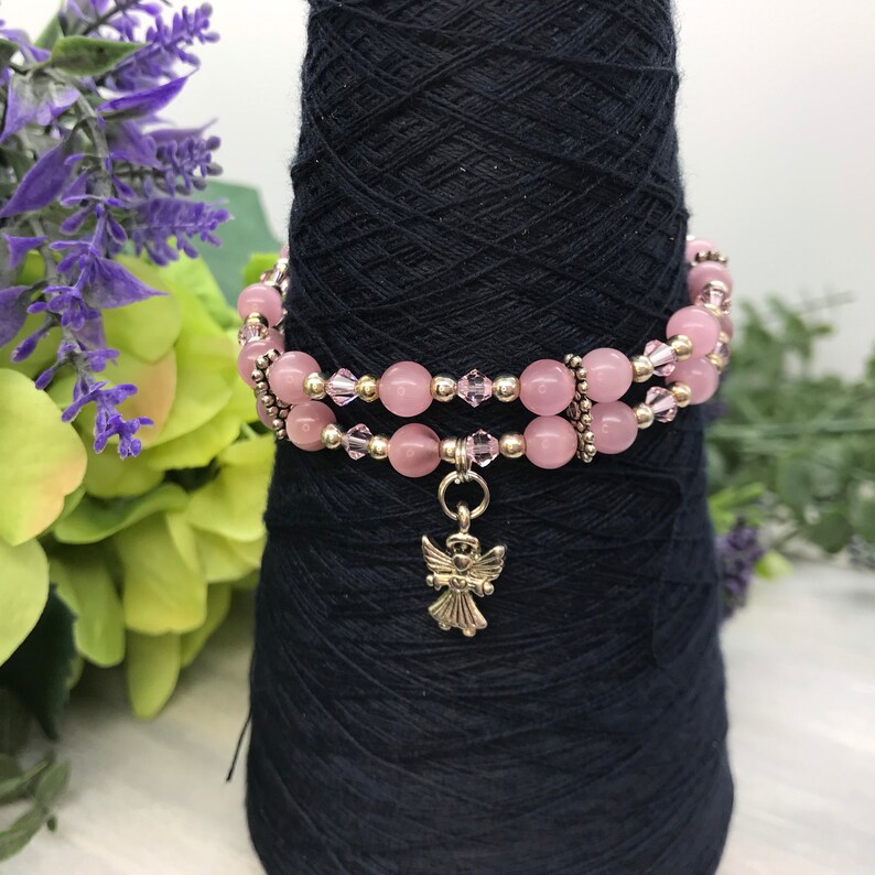 May include: A double-strand bracelet with pink beads and a silver angel charm. The bracelet is on a black spool.