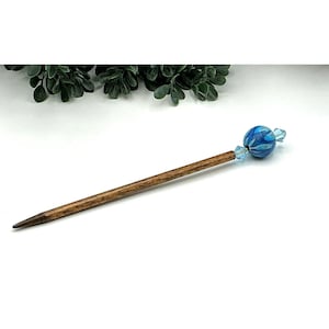 May include: A wooden hair stick with a dark brown finish. The top features a blue and white marbled bead and two blue crystal accents. The hair accessory is designed for decorative use.