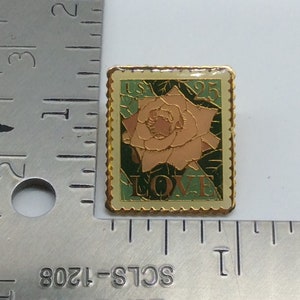 May include: A rectangular pin with a gold border, featuring a rose design. The pin has a light green background with the text "USA 25 LOVE". The rose is peach-colored with green leaves.
