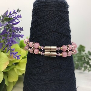 May include: A pink and silver beaded bracelet with a magnetic clasp. The bracelet is made with rose quartz and crystal beads.