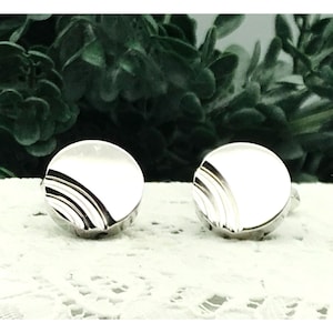 May include: A pair of silver cufflinks with a circular design featuring a series of concentric circles.