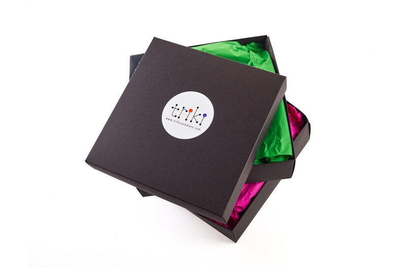 May include: Three black square boxes, partially open, revealing colorful tissue paper. The top box has a white circular sticker with the word "triki" and a colorful logo. The tissue paper is green and pink.