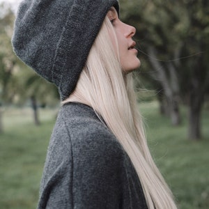 K&ouml;nnte beinhalten: Eine Frau mit langen blonden Haaren, die eine graue M&uuml;tze und einen grauen Pullover tr&auml;gt.