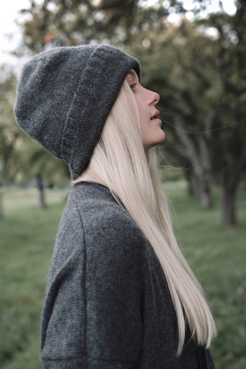 K&ouml;nnte beinhalten: Eine Frau mit langen blonden Haaren, die eine graue M&uuml;tze und einen grauen Pullover tr&auml;gt.