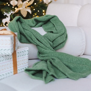 May include: A green knitted scarf draped over a white couch with a stack of wrapped gifts in the background.