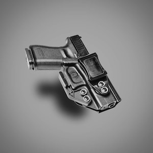 May include: Black handgun in a black holster. The holster has a belt clip and is secured with multiple screws. The gun has a textured grip and a magazine. The background is a solid gray.
